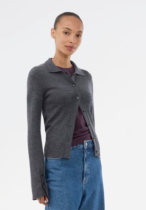 Grå ribbet cardigan med krave, knaplukning foran og lange ærmer. Båret over en mørkegrå top og sat sammen med blå højtaljede jeans.