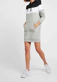 Grå hoodieklänning med svart och vit färgblockdesign, långa ärmar, framfickor och ribbad nederkant. Bärs med vita sneakers.