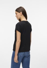 Camiseta negra de manga corta con las mangas remangadas, hecha de tela suave. Estilo con un corte holgado y combinada con vaqueros clásicos azules.