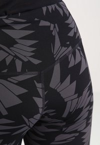 Lähikuva mustista legginsit, joissa on korkea vyötärö ja abstrakti harmaa geometrinen kuvio sekä näkyvät ompeleet.