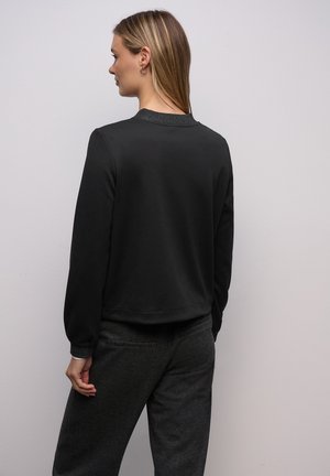 Černá mikina s hladkým povrchem a kulatým výstřihem, s dlouhými rukávy a mírně zkráceným střihem. Nositelná s tmavě šedými kalhotami.