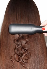 Des cheveux bruns lisses en cours de coiffage avec un lisseur à cheveux chauffant ghd max noir, une section montrant des boucles lâches.