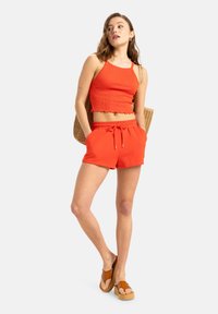 Röd ribbad croptop med scalloped nederkant, parat med röda shorts med dragsko. Modellen bär bruna platåskor och håller en flätad handväska.