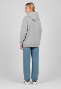 Felpa con cappuccio grigia chiara dal taglio morbido, abbinata a pantaloni blu larghi e sneaker bianche con strisce nere. Tessuto dalla texture morbida.