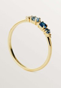 Anillo de oro con tres piedras ovaladas azules engastadas en garras, con una banda lisa y un acabado pulido que resalta el color y la claridad de las gemas.