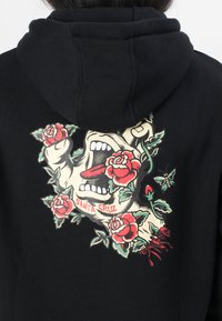Felpa nera con cappuccio caratterizzata da un audace design grafico di una bocca e rose. Colori vivaci rosso e verde con dettagli intricati e lettering "SANTA CRUZ."