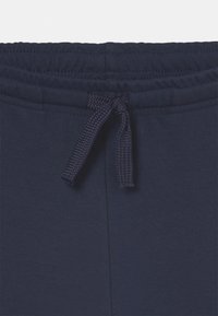 Pantaloni della tuta blu navy con un elastico piatto in vita e un cordino intrecciato. Texture liscia con dettagli di cucitura lungo il bordo.
