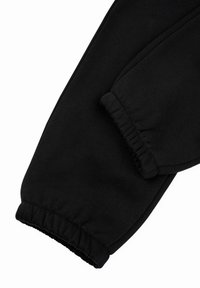 Pantaloni della tuta neri con una texture morbida, polsini elasticizzati e un design snello. Il tessuto è liscio e resistente con un colore uniforme.