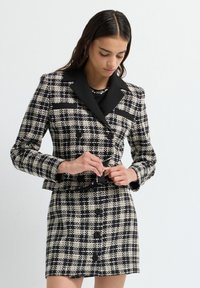 Blazer in tweed bianco e nero con colletto a revers e bottoni doppi, abbinato a una mini gonna coordinata con bottoni frontali.
