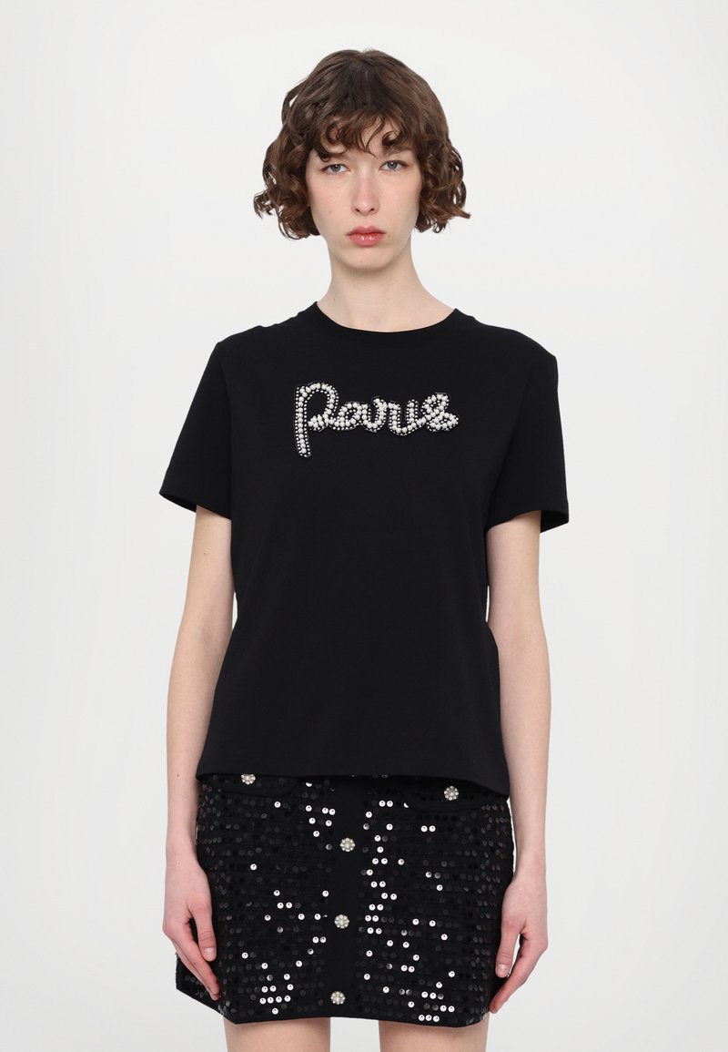 Schwarzes T-Shirt mit "Paris" aus Strass verziert, kurze Ärmel, kombiniert mit einem glitzernden schwarzen Rock, der eine strukturierte Oberfläche zeigt.