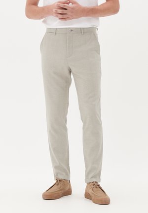 Light gray patterned trousers with a fitted design, featuring a single button closure and pockets, paired with beige, suede shoes.