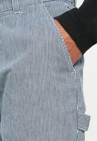 Striped pants in blue and white fabric, featuring a front pocket and a visible patch on the side, with a smooth texture.