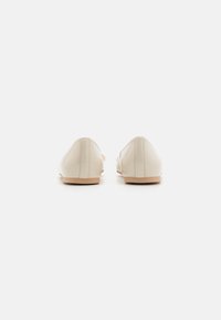 Sapatos de couro bege com um acabamento suave, bico fino e detalhe de costura mínima na parte de trás. Sola castanho claro.