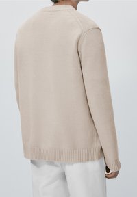 Cardigan en tricot beige avec poignets et ourlet côtelés, doté d'un col rond et d'un design simple et sans coutures. Texture lisse partout.