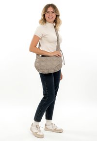 Quilted beige shoulder bag with a curved shape, featuring a braided strap and a smooth texture, displayed against a white background.