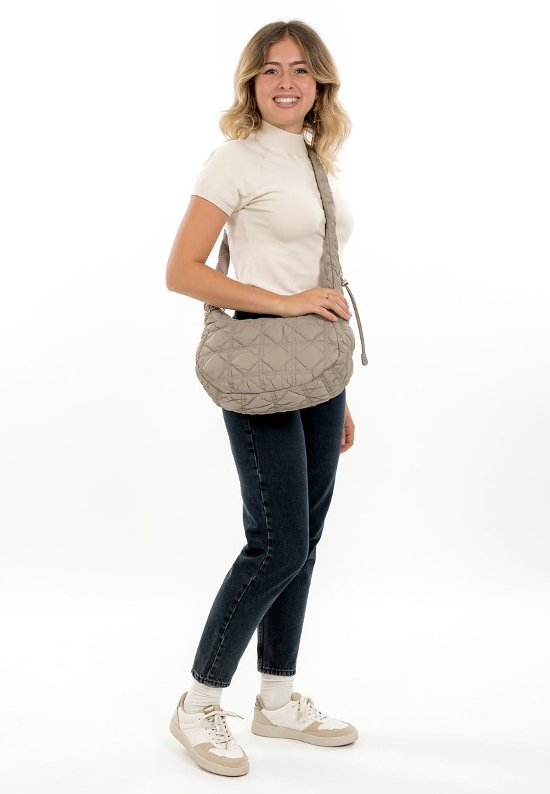Quilted beige shoulder bag with a curved shape, featuring a braided strap and a smooth texture, displayed against a white background.