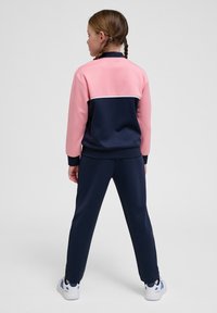 Conjunto de sudadera en color navy y rosa con un diseño en bloques de color; presenta mangas largas, puños de canalé y pantalones a juego. Acento blanco a lo largo de la espalda.