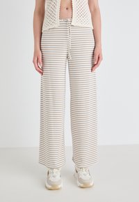 Gestreepte wijde broek in beige en gebroken wit, met een verstelbare tailleband en zachte, gestructureerde stof. Gekleed met chunky sneakers.