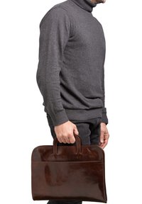 Bruine leren aktetas met twee handvatten, een gladde textuur, rechthoekige vorm en een voorvak, vastgehouden door een persoon in een grijze trui.