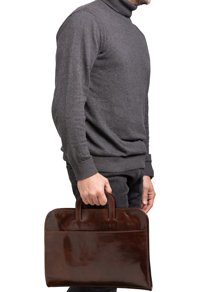 Bruine leren aktetas met twee handvatten, een gladde textuur, rechthoekige vorm en een voorvak, vastgehouden door een persoon in een grijze trui.