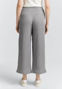 Pantalones de pierna ancha grises con un diseño texturizado y plisado. La cintura es elástica y tienen un ajuste relajado, combinados con zapatillas blancas.