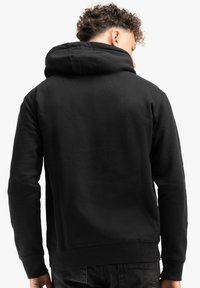 Sudadera con capucha negra de acabado texturizado, fabricada en una tela suave, con puños y dobladillo acanalados. Presenta un corte relajado y una capucha de tamaño medio.