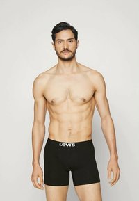 Melna boksa apakšveļa ar baltu "Levi's" logotipu jostasvietā, izgatavota no gludas auduma, ko valkā modelis ar sportisku augumu.