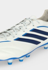 Λευκό παπούτσι ποδοσφαίρου με μπλε ρίγες Adidas και στασούνες, δεμένο, εμφανιζόμενο από μπροστινή-πλευρική γωνία σε απλό φόντο.