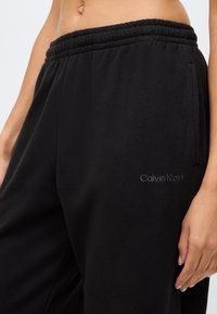 Juodos sportinės kelnių pagamintos iš minkštos medžiagos, su elastingu juosmeniu ir subtiliu "Calvin Klein" logotipu tamsesnio atspalvio šone.