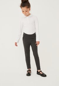 Graue dehnbare Hose mit schmaler Passform, ausgestattet mit einem Bund und seitlichen Taschen, kombiniert mit einem langärmeligen weißen Hemd mit Kragen und schwarzen Schuhen.