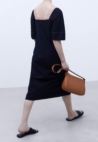 Robe en lin noire à manches courtes et dos carré, associée à un sac à main marron et des sandales noires sans bride. Texture lisse.