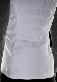 Top atletico bianco con pannello laterale testurizzato, caratterizzato da cuciture orizzontali, piccoli fori di ventilazione rotondi e un logo sull'orlo.