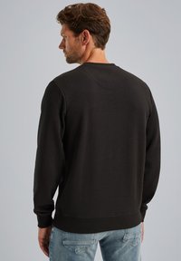 Sudadera negra hecha de algodón suave, con mangas largas, cuello redondo y dobladillo acanalado. La parte posterior presenta una textura suave con un detalle mínimo.