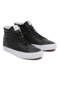 Mustat korkeavartiset tennarit, jotka on valmistettu sileästä nahasta, valkoisella kumipohjalla ja kohokuvioidulla tekstillä keskikohdassa. Klassinen nauhakiinnitys.