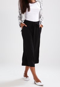 Svarta, vida byxor med dragsnöre i midjan och sidofickor, kombinerade med en vit topp och vita slip-on skor.