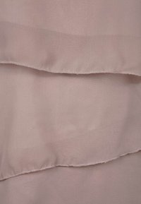 Trojílová tkanina v jemné prachové růžové, s třemi vrstvami a mírným třepením okrajů, což vytváří texturovaný vzhled. Hladký, lehký materiál.