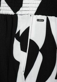 Černobílá látka s výrazným abstraktním vzorem. Elastický pas se pruhovaným detailem a malou viditelnou označovací štítkem.