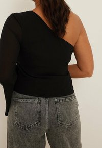 Svart asymmetrisk topp med en figurnära design och genomskinlig vänster ärm, i kombination med högmidjade grå jeans med bakfickor.