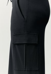 Svarta byxor med sidoficka. Tillverkade av slät, elastisk tyg. Har sömnadsdetaljer och en platt, öppen fickdesign.