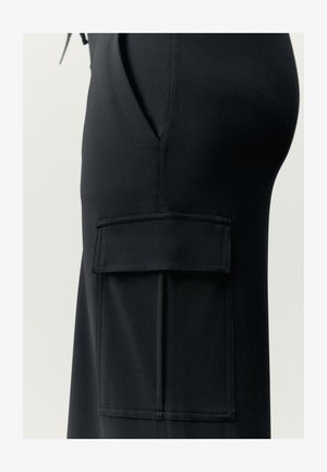 Čierne nohavice s bočnou kapsou. Vyrobené z hladkej, elastickej tkaniny. Obsahujú švy a plochý otvorený dizajn kapsy.