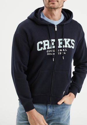 Marineblaue Zip-Hoodie aus Baumwollmischung, mit einer Fronttasche und kontrastierendem weißen und hellblauen Schriftzug auf der Brust.