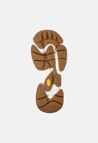 Suola di scarpa in gomma bianca e marrone con un design texturizzato caratterizzato da scanalature e un logo Vibram giallo. Forme curve e più sezioni visibili.