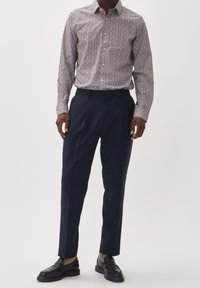 Camicia a maniche lunghe con motivo in colori chiari, abbinata a pantaloni neri su misura. Gli accessori includono mocassini neri e calzini a fantasia.