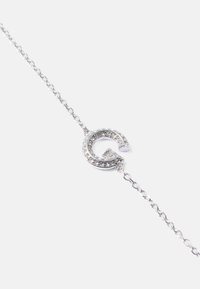 Silverarmband med en rund berlock prydd med en stiliserad "G" besatt med rhinestones, på en känslig kedja.