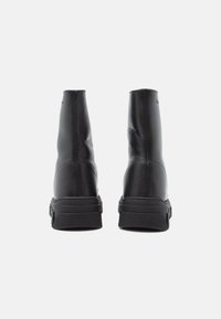 Bottines en cuir noir avec une texture lisse, dotées d'une semelle épaisse noire et de coutures minimales sur les côtés.