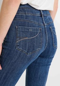 Jeans de mezclilla ajustados en azul oscuro con una textura suave, que cuentan con dos bolsillos traseros con costuras curvas y una cintura alta.