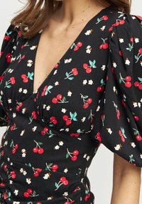 Schwarzes Kleid mit Kirsch- und Blumenmuster, ausgestattet mit Puffärmeln und einem V-Ausschnitt. Weicher Stoff mit einer gerafften Textur an der Taille.