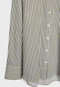 Camicia a maniche lunghe con righe verticali verde oliva e bianche, bottoni bianchi e polsini a righe orizzontali su uno sfondo bianco.