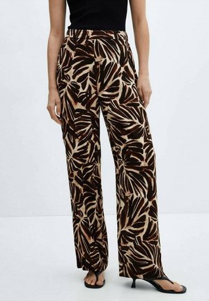 Vrouw draagt hooggetailleerde bruine en beige wijde broek met bladmotief, een zwart mouwloos topje en zwarte sandalen met hak.