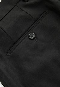 Schwarzer Stoff mit flacher Frontgestaltung, seitlicher Tasche und einem einzelnen schwarzen Knopf. Die Textur wirkt glatt mit einem dezenten Finish.